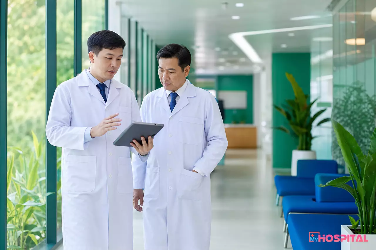 Bác sĩ cầm máy tính bảng đi cùng trưởng khoa trên hành lang khối phòng khám để xem báo cáo hiệu suất bác sĩ