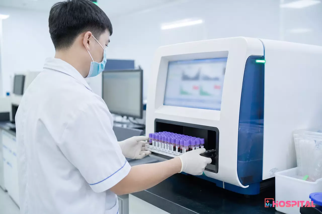 Kỹ thuật viên đặt khay mẫu máu vào máy phân tích huyết học trong phòng xét nghiệm