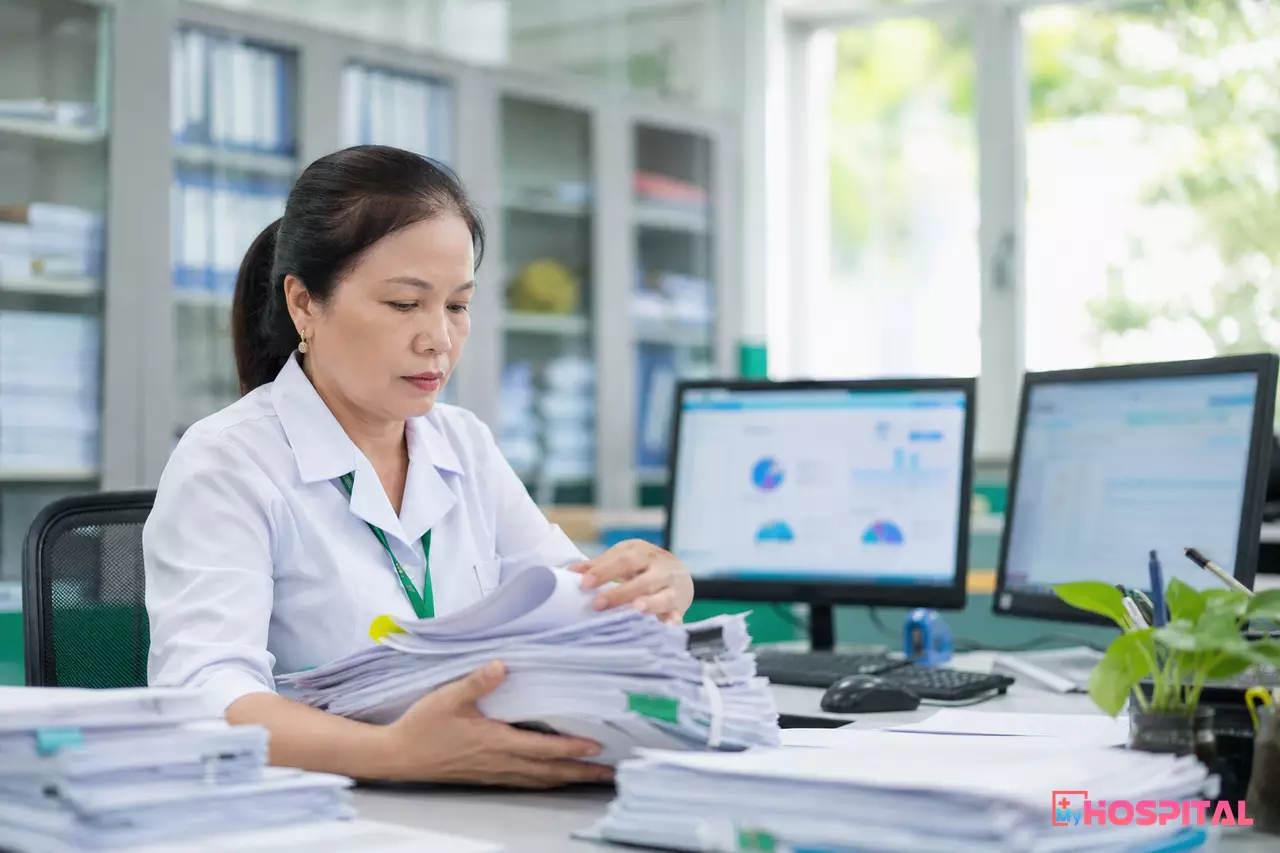 Nhân viên kế toán BHYT đối chiếu hồ sơ giấy với dữ liệu trên máy tính tại phòng tài chính bệnh viện
