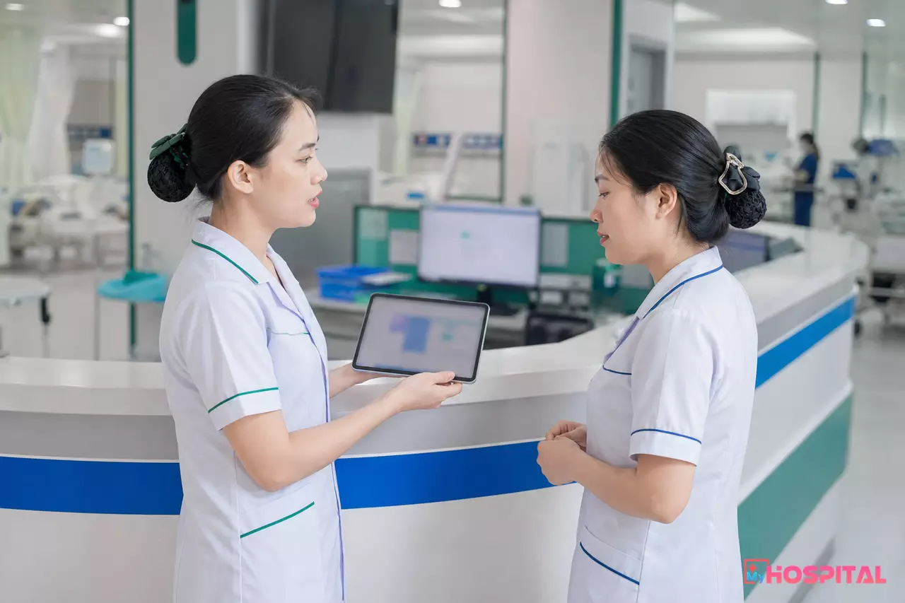 Hai điều dưỡng ca sáng và ca đêm bàn giao người bệnh cạnh quầy điều dưỡng