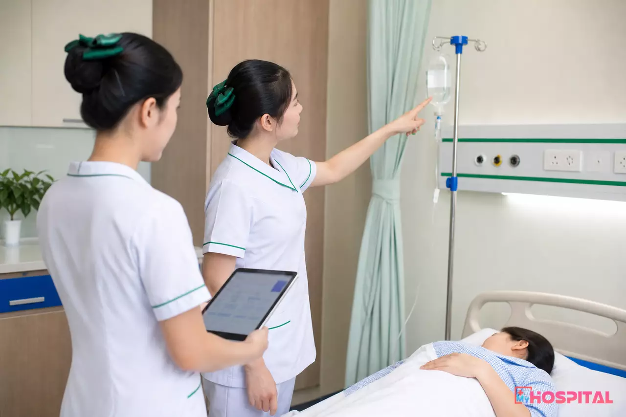 Điều dưỡng đối chiếu túi dịch truyền và máy tính bảng bàn giao bên giường người bệnh