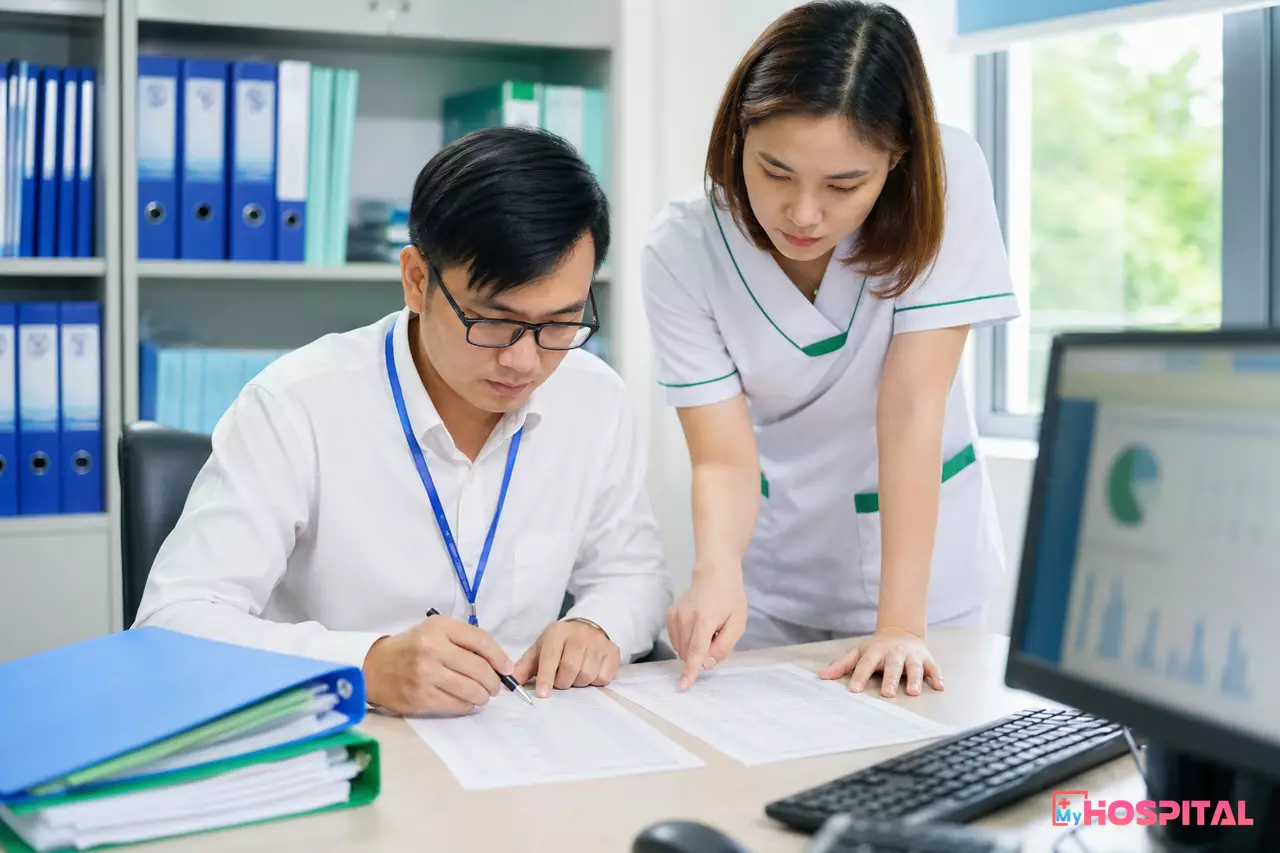 Nhân viên phòng kế hoạch tổng hợp đối chiếu bảng chuyển đổi mã dịch vụ kỹ thuật cũ và mới trên giấy trước khi cập nhật hệ thống