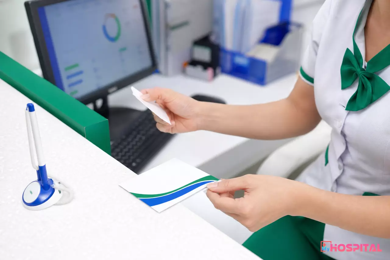 Cận cảnh nhân viên tiếp đón đối chiếu giấy khai sinh với thẻ BHYT trẻ em trên bàn quầy tiếp đón
