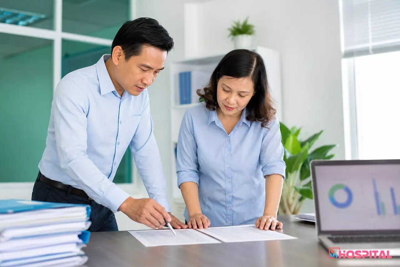 Kế toán viện phí đối chiếu quyết định giá mới với danh mục dịch vụ kỹ thuật trên bàn làm việc