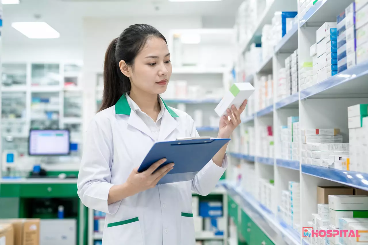 Dược sĩ kiểm tra hộp thuốc trên kệ và đối chiếu với danh sách trên bảng kẹp giấy trong kho dược bệnh viện