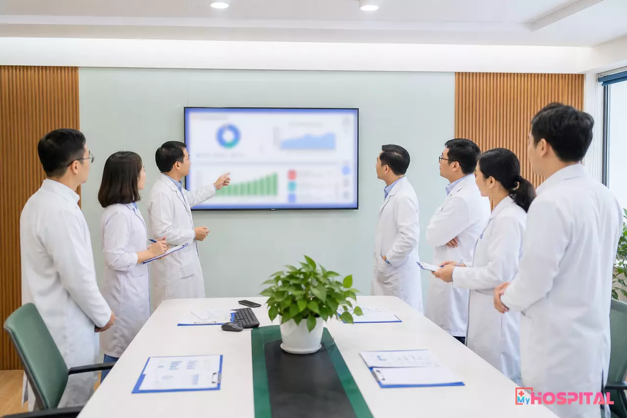Giám đốc và các trưởng khoa trao đổi quanh màn hình số liệu trong buổi giao ban đầu tuần