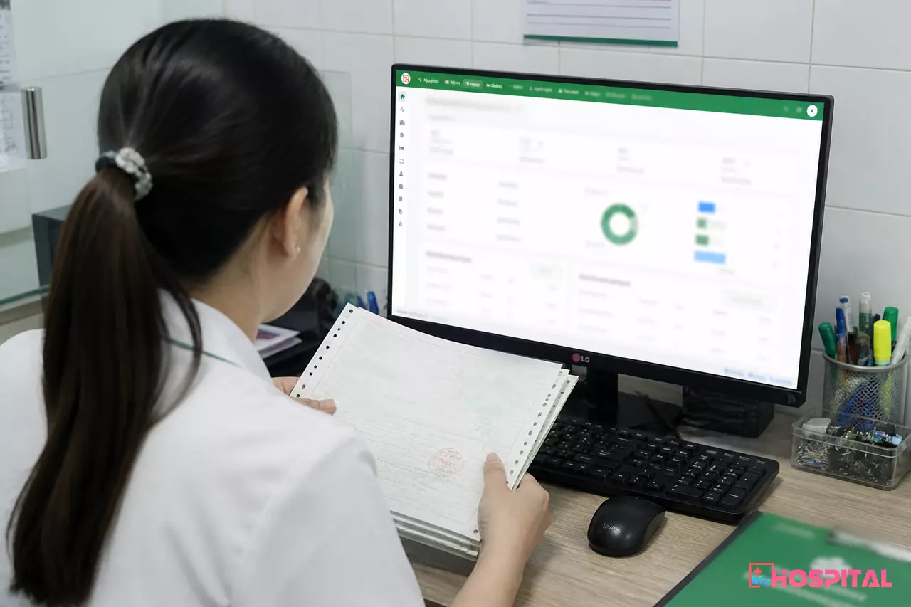Kế toán viện phí đối chiếu phiếu thu với báo cáo công nợ trên máy tính
