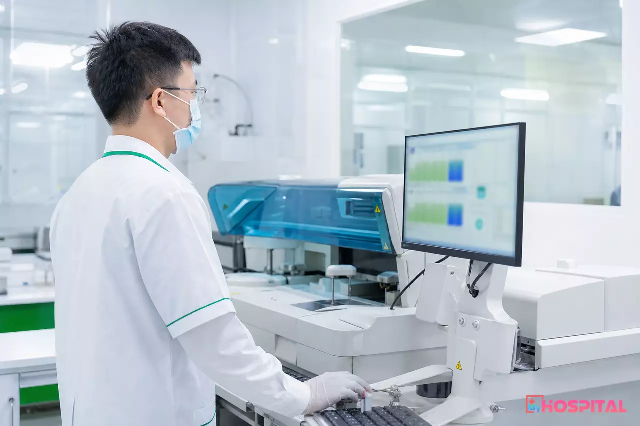 Kỹ thuật viên xét nghiệm kiểm tra kết quả từ máy xét nghiệm sinh hóa tự động trước khi duyệt về hồ sơ người bệnh