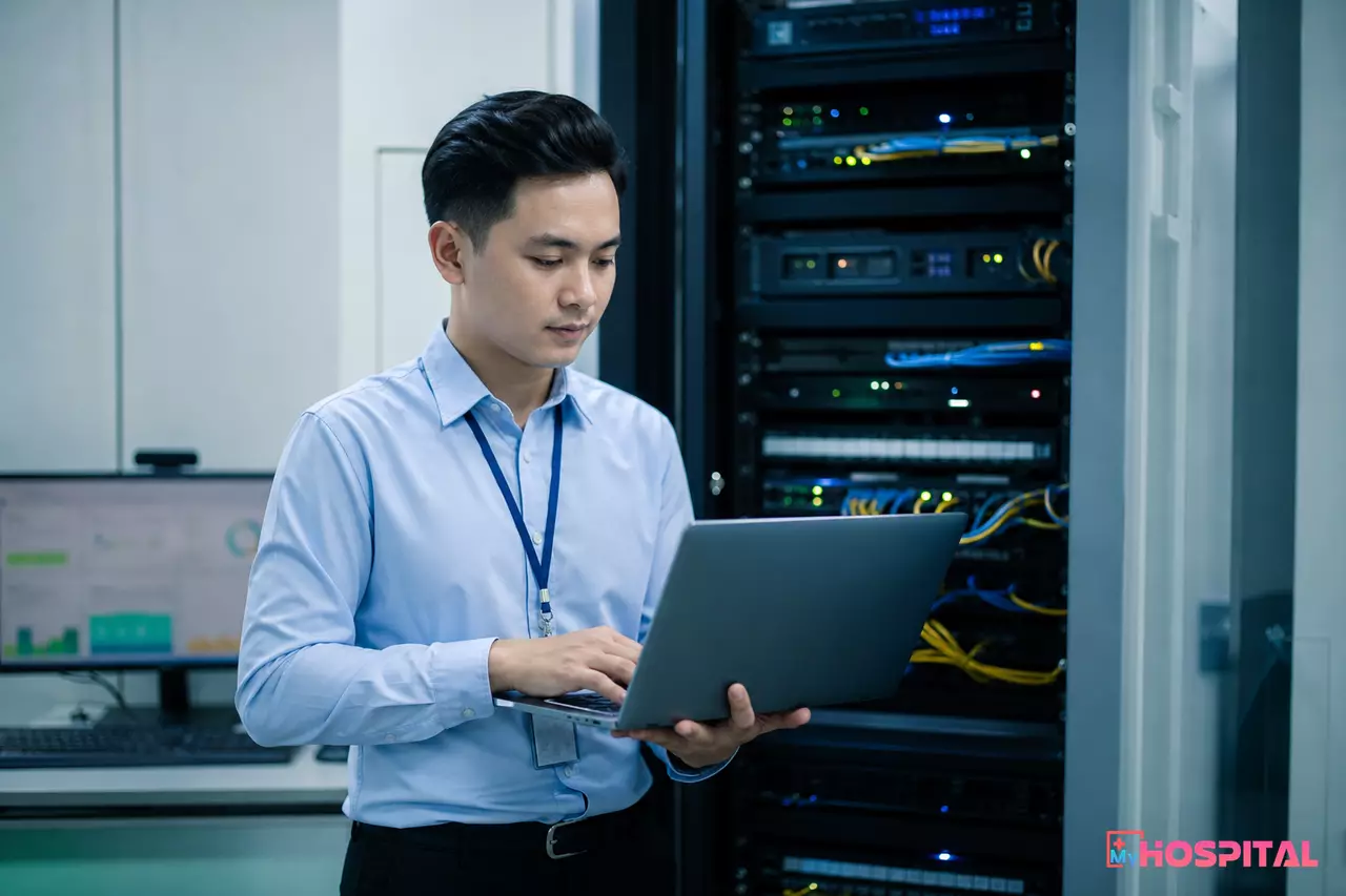 Nhân viên CNTT bệnh viện kiểm tra thiết bị trong phòng máy chủ với tủ rack và dây cáp mạng