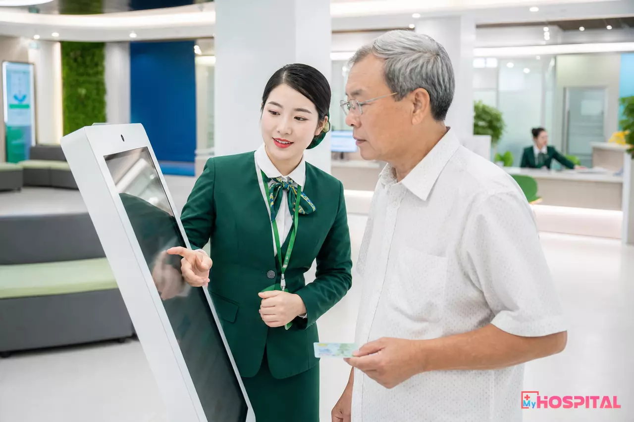Nhân viên tiếp đón hướng dẫn người bệnh đăng ký khám qua kiosk tại bệnh viện
