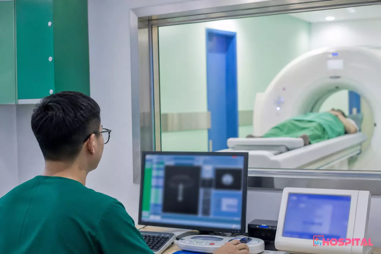 Kỹ thuật viên ở phòng điều khiển máy CT nhìn vào phòng chụp có người bệnh