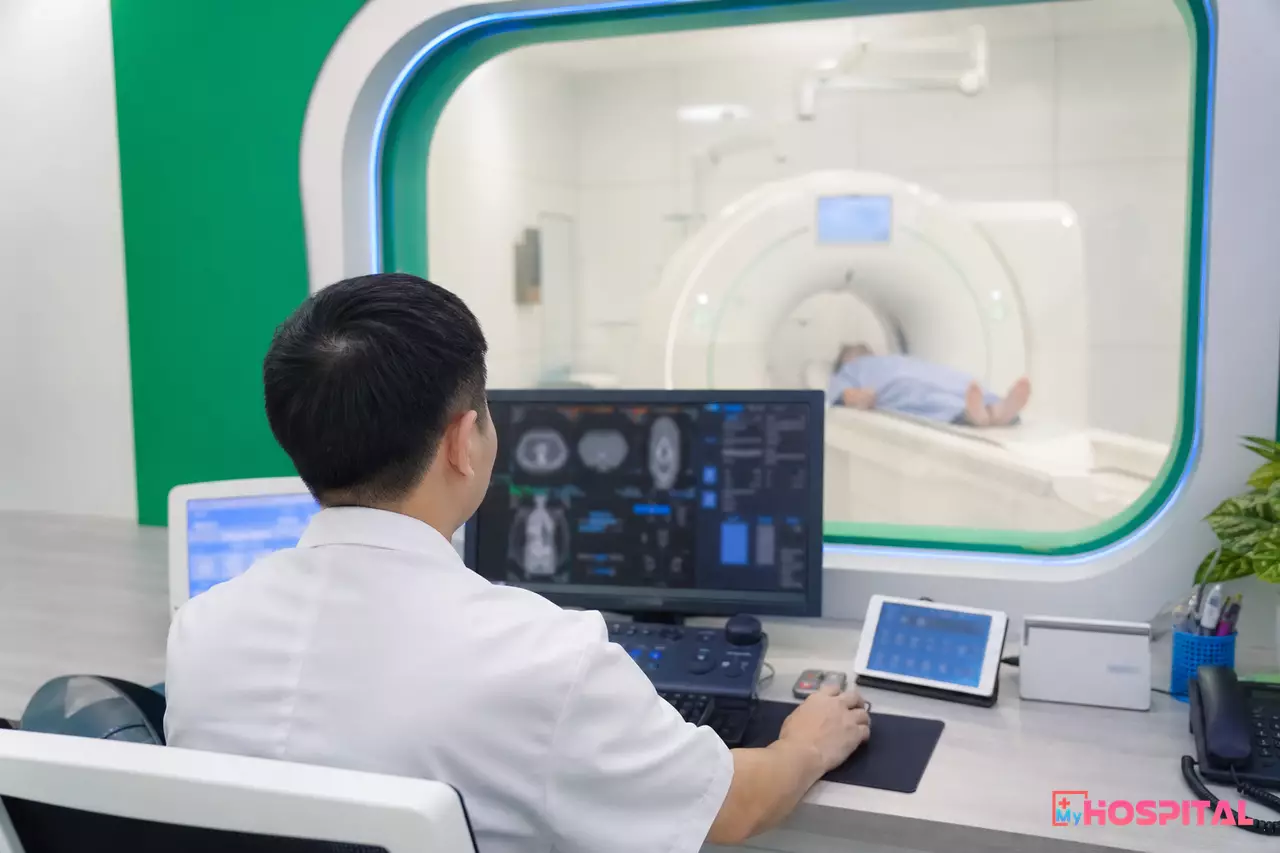 Kỹ thuật viên điều phối ca chụp CT tại phòng điều khiển, người bệnh nằm trên bàn máy bên trong