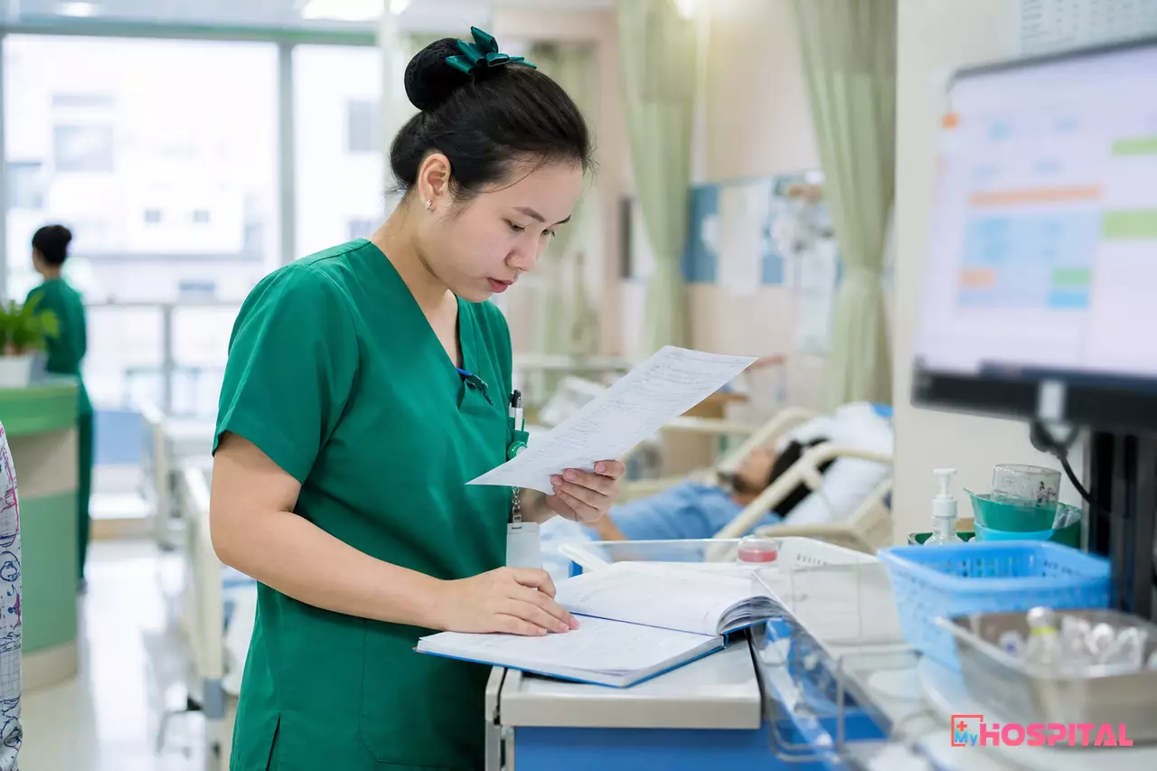 Điều dưỡng cầm tờ y lệnh viết tay đối chiếu với sổ thực hiện thuốc tại buồng bệnh