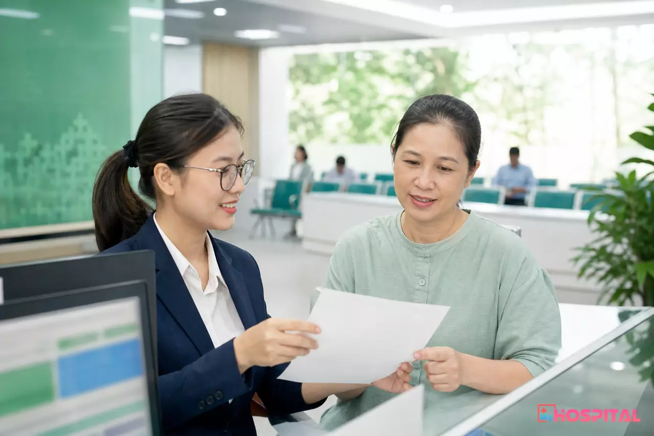 Nhân viên thu ngân viện phí đưa bảng kê chi phí ra viện cho người nhà người bệnh tại quầy thu ngân