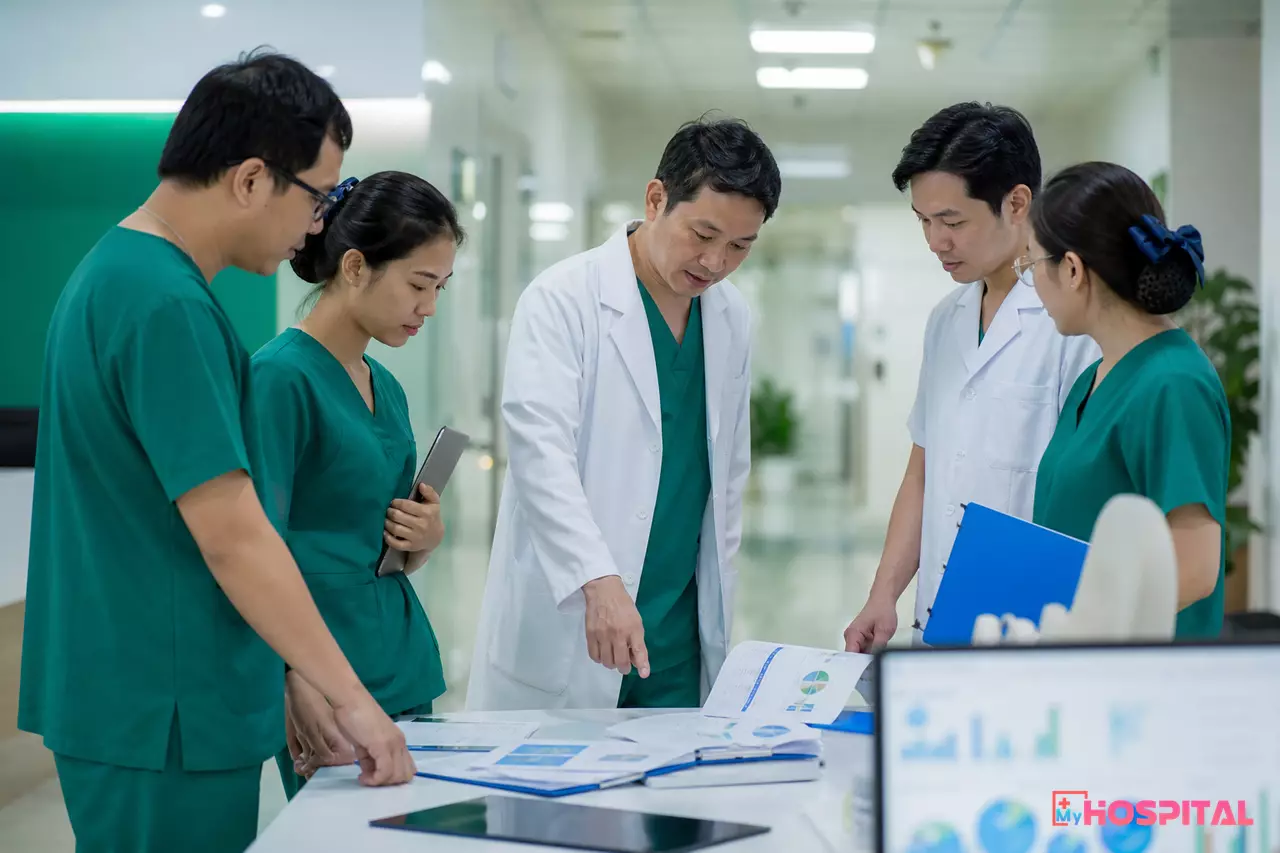 Buổi giao ban đầu tuần ở bệnh viện, trưởng khoa trao đổi với các bác sĩ và điều dưỡng trưởng quanh bản in báo cáo