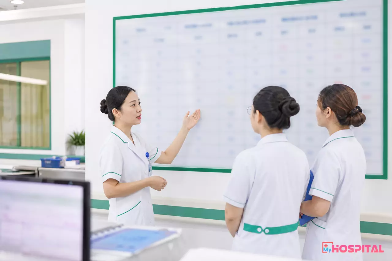 Điều dưỡng trưởng và điều dưỡng viên trao đổi trước bảng phân công ca trực của khoa khám bệnh